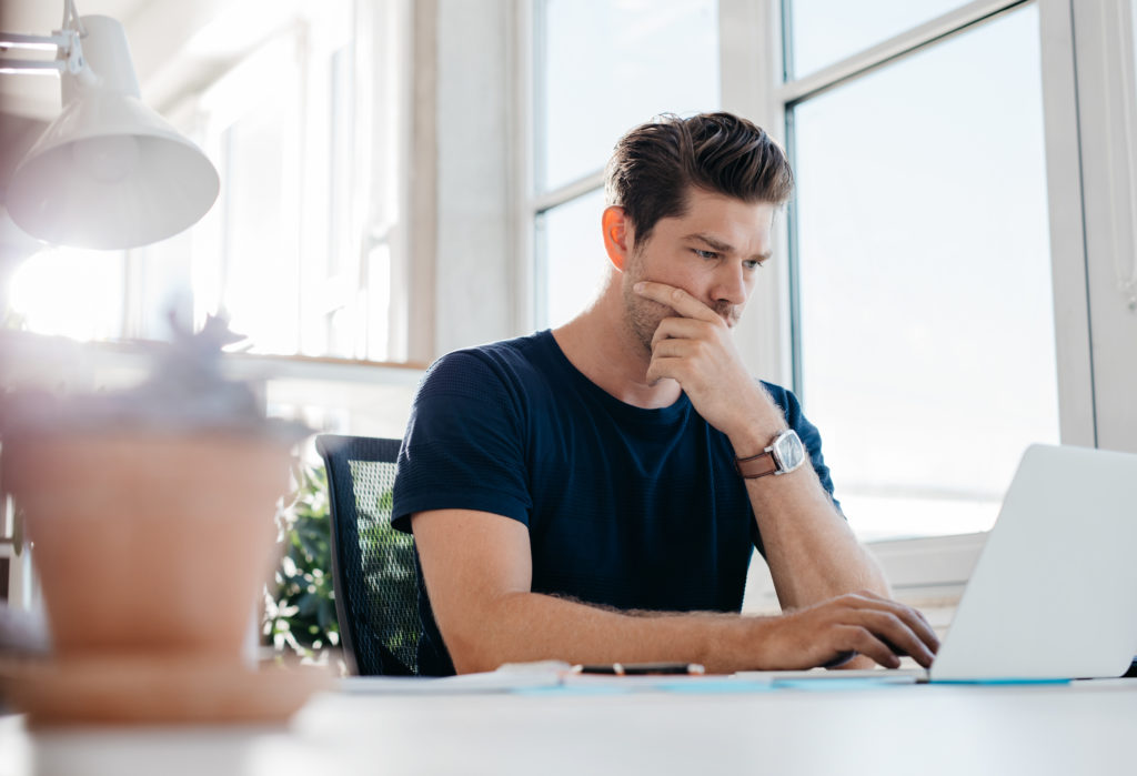 Pensive young male executive using laptop at his desk